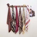 Gedrapeerde sjaals in verschillende prints en kleuren, waaronder een rood-witte sjaal met landschapsprent, aan een houten rek.