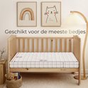 Een 60x120 cm babymatras van 15 cm dik in een houten ledikant, naast een nachtkastje met een teddybeer.