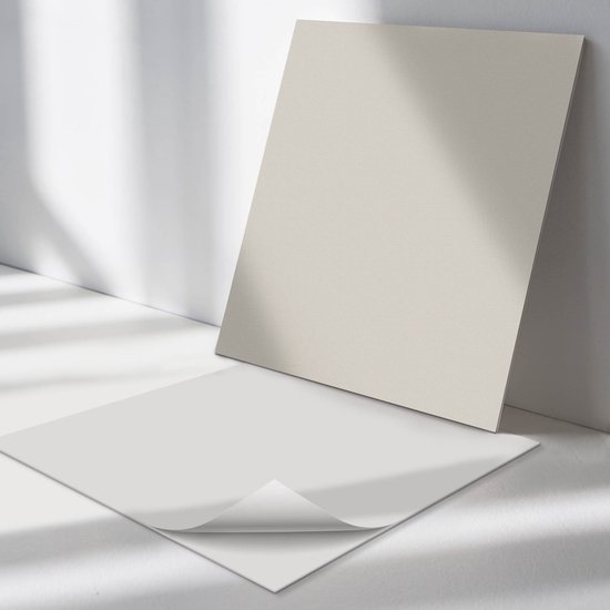 Twee lichtbeige, matte tegels liggen op een witte ondergrond, een ervan met een omgevouwen hoek.