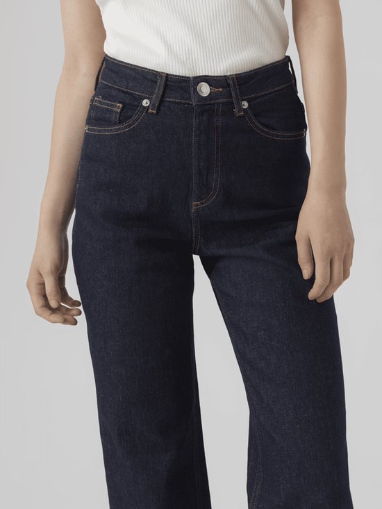 Gedetailleerde voorkant van donkerblauwe jeans met wijde pijpen en oranje stiksels.