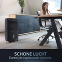 Zwarte mobiele aircooler op de achtergrond terwijl een vrouw aan een bureau zit, schone lucht dankzij de ionisator.