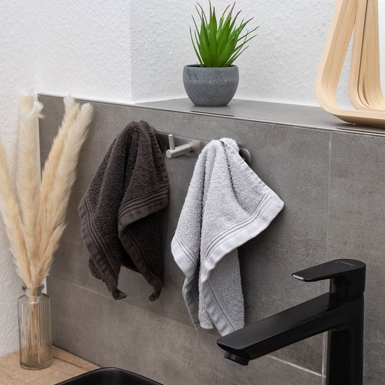 Un portemanteau en acier inoxydable à 3 crochets sur un mur carrelé gris, avec deux serviettes et un robinet.
