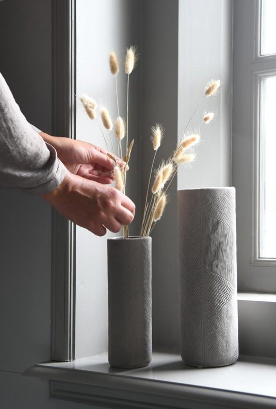Twee taupekleurige vazen met geometrisch reliëfpatroon, één met gedroogde bloemen.