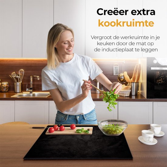 Vrouw snijdt kruiden op een zwarte inductiebeschermer die op een aanrecht ligt.