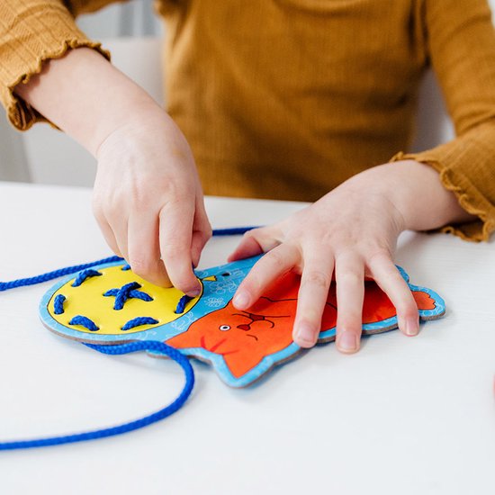 Kind rijgt blauw koord door geel-blauw schuurpapiertje met kattenkop