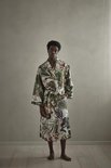 Model staat recht, gekleed in een lichte badjas met veelkleurige jungleprint van bladeren en dieren.