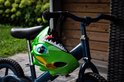 Groene dino fietshelm hangend aan een kinderfiets.