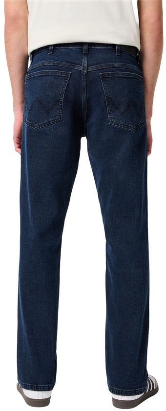 Achterkant van een man in een donkerblauwe spijkerbroek met Wrangler logo op de achterzakken.
