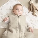 Baby in een zandkleurige, gevoerde slaapzak met rits. Ligt op een laken met takjesprint.
