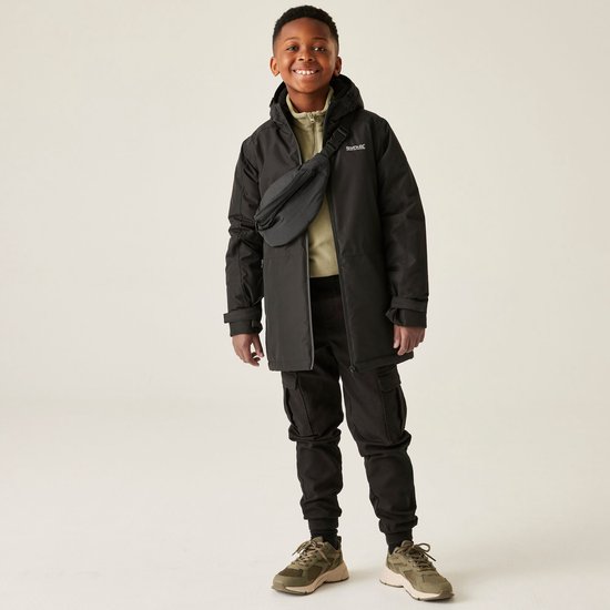 Jongen in zwarte jas met capuchon, heuptas, cargo broek en sneakers.