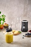 Een groene smoothie in een beker met rietje, naast de zwarte Fritel blender en verse ingrediënten zoals blauwe bessen en mango.