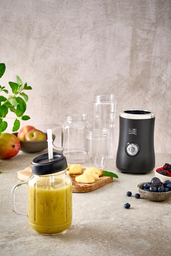 Een groene smoothie in een beker met rietje, naast de zwarte Fritel blender en verse ingrediënten zoals blauwe bessen en mango.