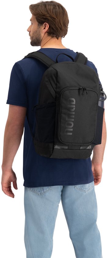 Man met donkerblauwe t-shirt en spijkerbroek draagt zwarte rugzak.