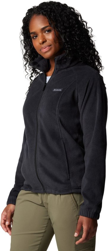 Model draagt een zwarte Columbia fleece trui met rits, lichtblauwe top en olijfgroene broek.