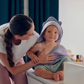 Een jongen met een lichtpaarse, met berenoren versierde badcape met capuchon, zit op een commode bij zijn moeder.
