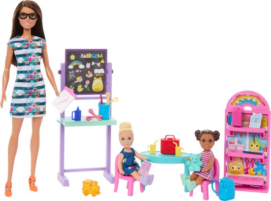 Barbie pop met een gestreepte jurk, bij een schoolbord, tafel en boekenrek. Twee Chelsea poppen zitten aan tafel.