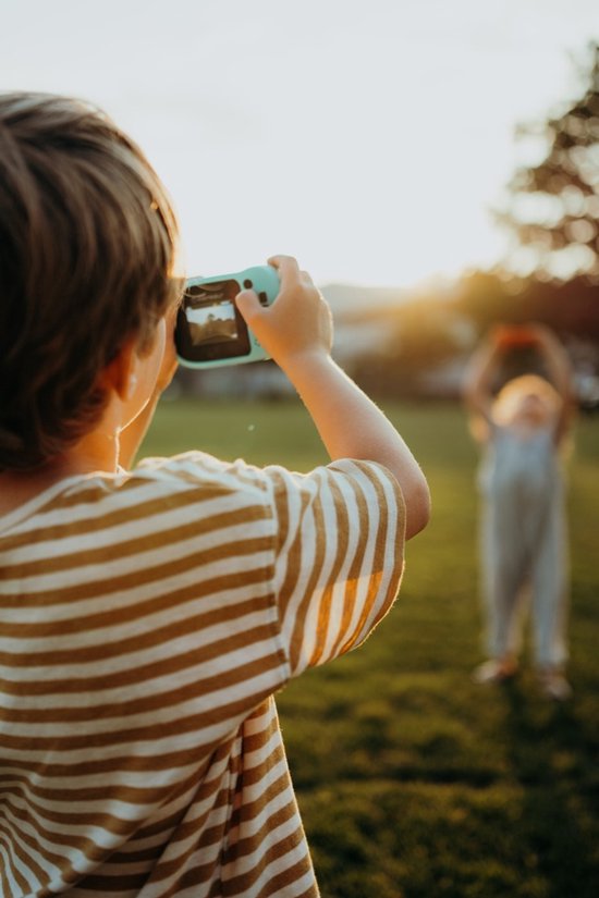 Jongen met een gestreept shirt neemt een foto met een cyaan Kidycam camera.
