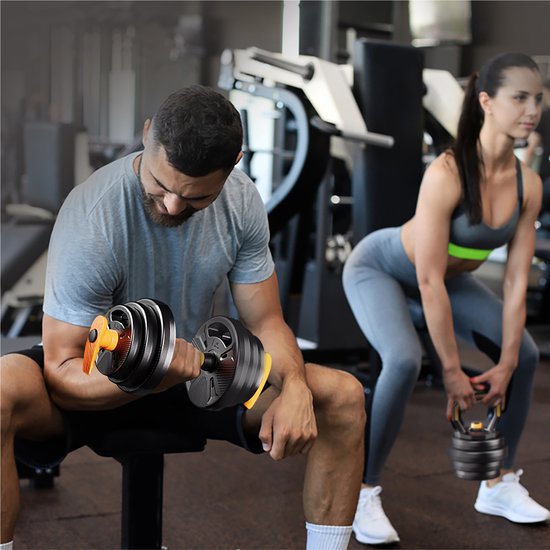 Man zit op een bankje met een dumbbell, vrouw doet een squat met een kettlebell in de sportschool.