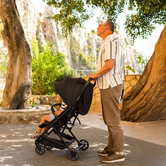 Man met gestreept shirt duwt zwarte Deryan buggy met kind in park.
