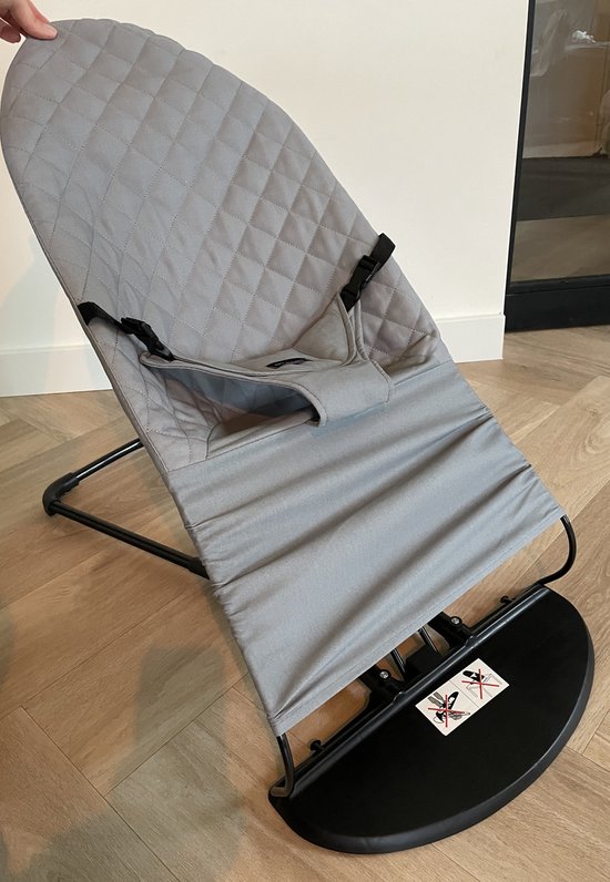 Grijze, gewatteerde stoelhoes voor een wipstoel op een houten vloer. Zwart frame en basis.