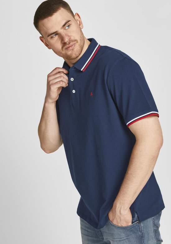 Man met donkerblauw poloshirt met rode/witte kraag- en mouwboorden en rode logo op borst.