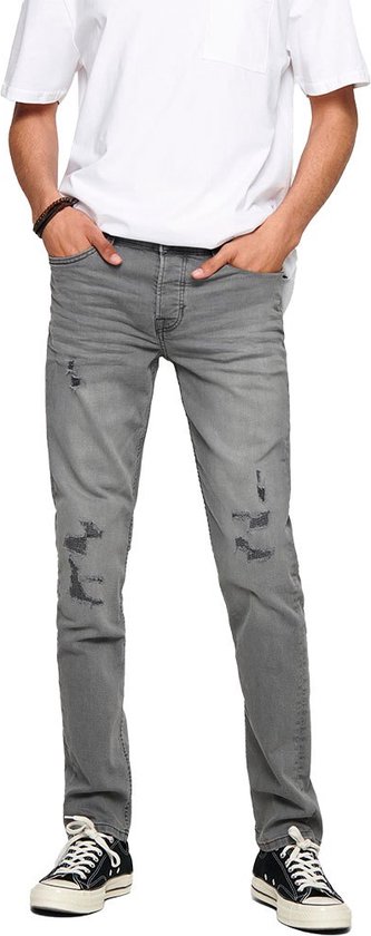 Grijze skinny jeans met scheuren op de knieën, gedragen door een man met een wit T-shirt.