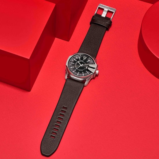 Zilverkleurig Diesel horloge met donkerbruine leren band, op een rode achtergrond met rode kubussen.