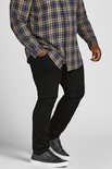 Man met geruite blouse en zwarte jeans, zijaanzicht.
