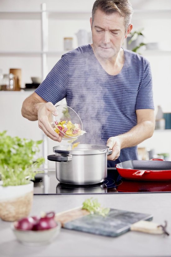 Man in gestreept T-shirt voegt gekleurde pasta toe aan dampende zilverkleurige kookpot.