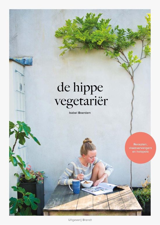 Vrouw in gestreept vest zit aan tafel, leest boek met titel 'de hippe vegetariër'.