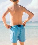 Jongetje staat aan het strand, met de rug naar de camera, draagt een lichtblauwe zwembroek met 'SEA'S' label.