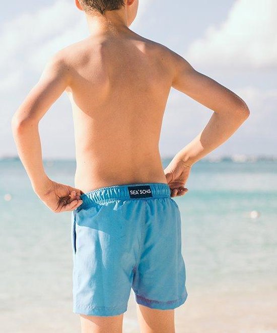 Jongetje staat aan het strand, met de rug naar de camera, draagt een lichtblauwe zwembroek met 'SEA'S' label.