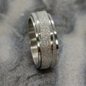 Zilverkleurige ring met een glinsterende, gestreepte band, gedraaid op een marmeren achtergrond.