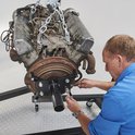 Un homme en chemise bleue attache un moteur lourd à un support moteur noir avec des outils.