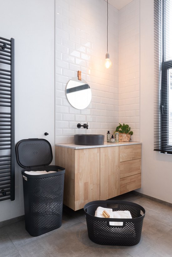Antracietgrijze Curver Infinity wasmand met deksel in badkamer met houten meubel en radiator.