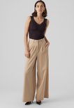 Model draagt zwarte top met kanten schouderbandjes en beige wijde broek met hoge taille.
