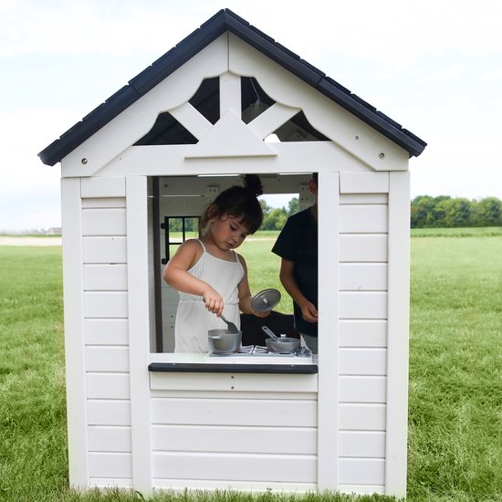 Meisje in wit speelhuisje speelt met kookgerei in de speelkeuken. Op de achtergrond een jongen.
