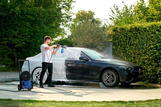 Man spuit schuim op een zwarte auto met een blauwe Nilfisk hogedrukreiniger in een tuin.