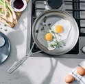 Twee gebakken eieren met lente-ui in een zilverkleurige pan op een gasfornuis.
