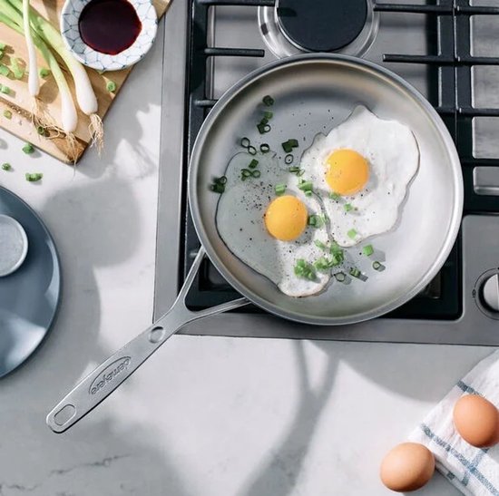Twee gebakken eieren met lente-ui in een zilverkleurige pan op een gasfornuis.