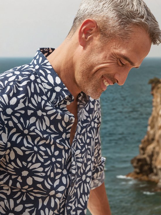 Close-up van een lachende man in donkerblauw overhemd met witte bloemenprint.