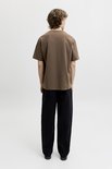 Man van achteren gezien in een effen bruin t-shirt met korte mouwen en zwarte broek.