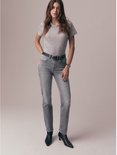 Model in een grijs t-shirt, grijze jeans met zwarte riem en zwarte enkellaarsjes.
