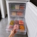 Open vriezerlade met bevroren zalm, kip, gehakt, worstjes, erwten en andere groenten.