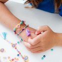 Close-up van een kinderarm met twee armbandjes, versierd met gekleurde kralen en tassels. Een paarse tassel hangt aan één armband.