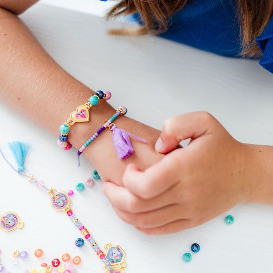 Close-up van een kinderarm met twee armbandjes, versierd met gekleurde kralen en tassels. Een paarse tassel hangt aan één armband.