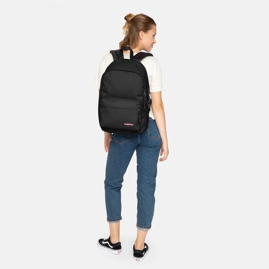 Sac à dos Eastpak noir avec compartiment pour ordinateur portable, porté par une femme en jean bleu et t-shirt blanc.