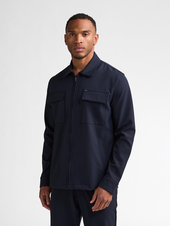 Man in donkerblauw jack met rits, twee borstzakken en opstaande kraag.