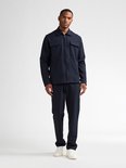 Man in donkerblauw jack met rits, twee borstzakken en bijpassende broek.