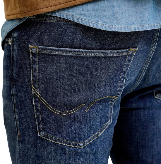 Close-up van de achterzak van een donkerblauwe spijkerbroek met gele stiksels.